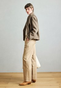 Pruun villane bleiser, hele beež puuvillased püksid ja beežid nahast pahkluu saabid. Komplekt on lõdva lõikega ja sisaldab dekoratiivseid taskuid.