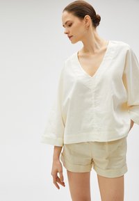 Løs passende v-hals bluse i lys creme linned, med brede ærmer og lige kant, parret med matchende beige shorts.