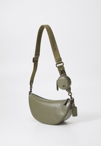 Borsa a spalla in pelle verde con design curvo, dotata di una pochette rotonda removibile e di una tracolla testurizzata con il marchio "COACH".