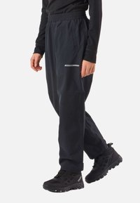 Person wearing black elastic-waist outdoor pants with side pockets and black hiking shoes, standing with one foot slightly raised.