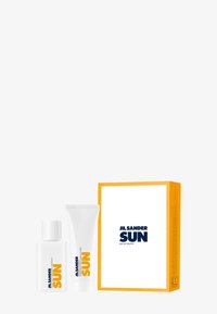 Conjunto de fragancia JIL SANDER SUN, que presenta una botella transparente y un tubo blanco. El embalaje es blanco con un acento amarillo brillante y un texto azul en negrita.