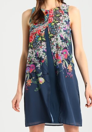 Robe bleu marine sans manches avec un motif floral coloré sur le haut, présentant une fente frontale sur une doublure bleu marine unie.