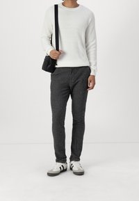 White ribbed sweater, grey textured trousers, and white sneakers with black stripes. Black crossbody bag adds contrast.