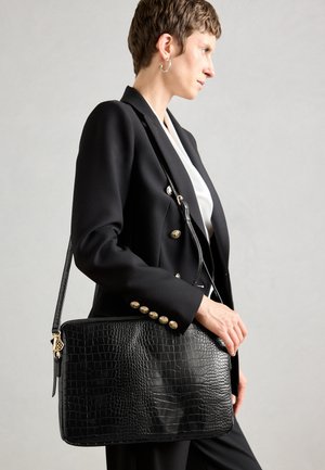 Borsa nera in pelle con stampa alligatore, dal texture morbido, dotata di chiusura con zip e di una tracolla removibile. Accenti in metallo dorato visibili.