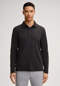 Schwarzes Langarm-Polohemd mit Kragen, Knopfleiste und dezentem Logodetail. Der Stoff wirkt glatt und dehnt sich sanft.