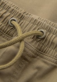 Gros plan d'une ceinture élastique beige avec un cordon tressé passé à travers des œillets métalliques sur un tissu en coton.