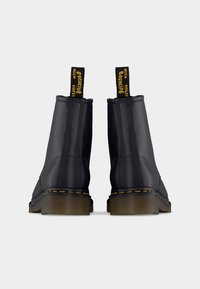 Sorte ankelstøvler med glat finish, gule syninger og træksnore med tekst. Kraftige, teksturerede såler fuldender designet.