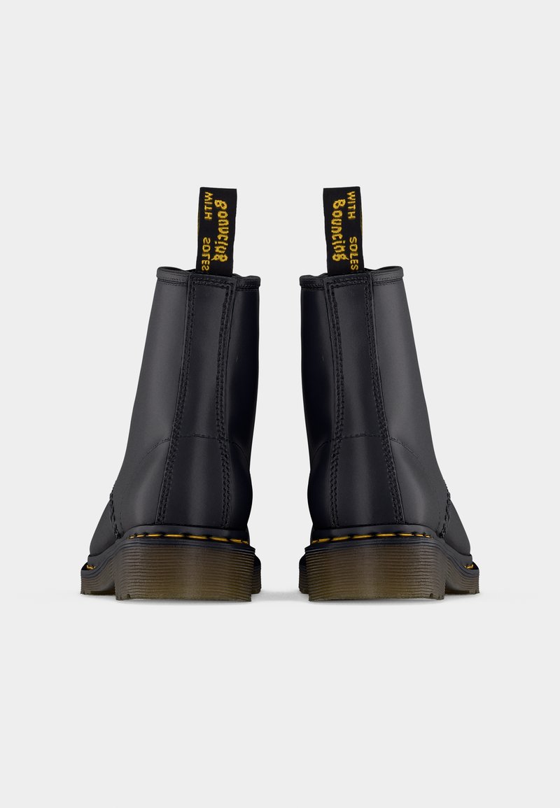 Sorte ankelstøvler med glat finish, gule syninger og træksnore med tekst. Kraftige, teksturerede såler fuldender designet.