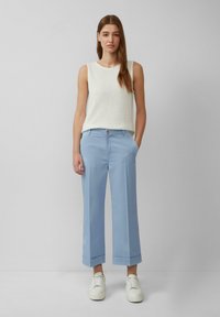 Top bianco senza maniche con finitura testurizzata, abbinato a pantaloni larghi blu chiaro con orlo cucito e tasche frontali. Sneakers bianche.