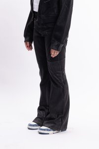 Μαύρο τζιν παντελόνι με φαρδιά γραμμή, λεία υφή και υποτόνους λεπτομέρειες, συνδυασμένο με λευκά και μπλε χαμηλά αθλητικά παπούτσια.