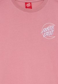 Šviesiai rožinė medvilninė marškinėlių su apvaliu kaklu, su baltu ir rožiniu "Santa Cruz" logotipu kairėje krūtinės pusėje.