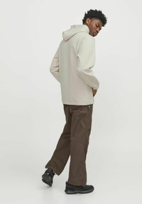 Jachetă cu glugă de culoare gri deschis, cu o croială lejeră, asortată cu pantaloni de culoare maro închis. Jacheta are manșoane elastice și buzunare laterale, iar pantalonii sunt drepti.