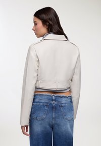 Giacca in pelle bianca corta con colletto classico e chiusura frontale con bottoni, abbinata a jeans in denim a vita alta con orlo sfrangiato.