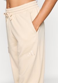 Bézs melegítőnadrág puha tapintással, elasztikus derékpánttal, húzózsinórral, oldalzsebekkel és egy kis hímzett logóval.