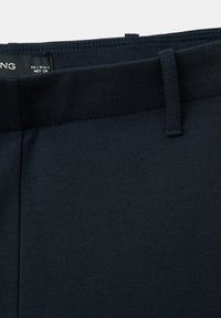 Mørkeblå, teksturerede stofbukser med livrem og bæltestrop, og en synlig størrelseslabel indeni.