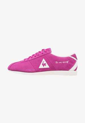 Zapatilla baja de ante rosa con suela blanca, logo triangular con un gallo y texto "Le coq sportif" en el lateral.