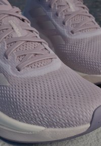 Zapatillas deportivas de color púrpura claro con una parte superior de malla texturada, cierre de cordones prominente y suela de goma. Presenta detalles sutiles del logo y acentos suaves.
