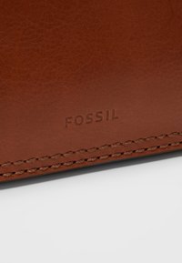Surface en cuir marron avec "FOSSIL" embossé au-dessus d'une couture cousue sur un fond clair.
