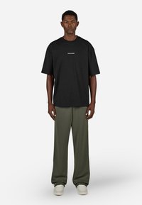 Black cotton t-shirt with short sleeves and a round neck, featuring white text. Paired with loose-fitting olive green trousers and white sneakers.