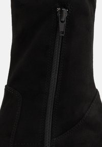 Botte de cheville en daim noir avec fermeture éclair sur le côté, texture lisse et coutures détaillées le long de la couture pour un design structuré.
