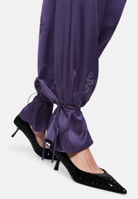 Purple satin trousers with tapered cuffs and drawstrings, paired with black sequined pointed-toe heels featuring a slim heel.