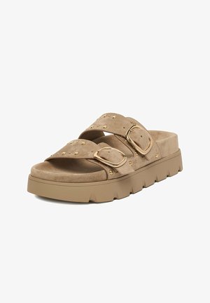 Sandalia plana beige de ante con suela gruesa de goma, doble tiras con grandes hebillas doradas y pequeñas tachuelas doradas.