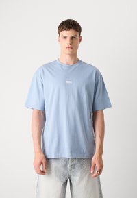 Ljust blå bomull t-shirt med rund hals, korta ärmar och en tryckt logotypetikett i mitten, i par med bleka grå jeansshorts.