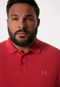 Rode polo t-shirt met een gestructureerde afwerking, voorzien van een drieknoopsluiting en een klein, ton sur ton geborduurd logo op de borst.