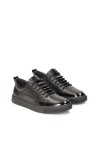 Zapatillas de cuero negro con patrón en relieve, acentos brillantes, punta redonda y suela de goma plana. Presentan cordones negros y una lengüeta trasera.