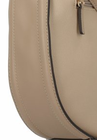 Sac à main en cuir beige avec une finition texturée, présentant une forme incurvée, des coutures contrastées sombres et un détail de poche zippée.