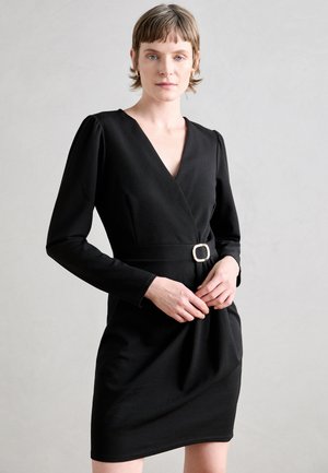 Robe portefeuille noire avec des manches longues, décolleté en V et une taille cintrée, ornée d'une boucle de ceinture carrée en métal doré. Tissu lisse, coupe ajustée.