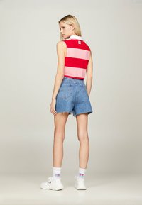 Rød- og lyserødstripet ærmeløs top med en hvid krave, parret med højtaljede denimshorts med en rå kant. Hvide sneakers.