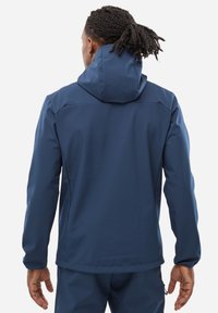Veste imperméable bleu marine avec capuche ajustée, manches longues et tissu texturé ; les caractéristiques comprennent une finition lisse et des coutures minimales.