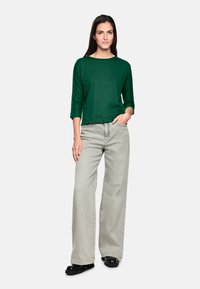 Grünes, langärmeliges Oberteil mit quadratischem Ausschnitt, kombiniert mit hellgrauen, weitem Hosen und schwarzen Plateauschuhen.