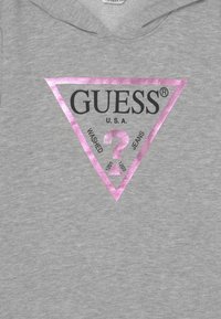 Felpa grigia con cappuccio caratterizzata da un grande logo triangolare rosa con la scritta "GUESS", U.S.A., e "WASHED JEANS" in nero. Texture morbida, design casual.
