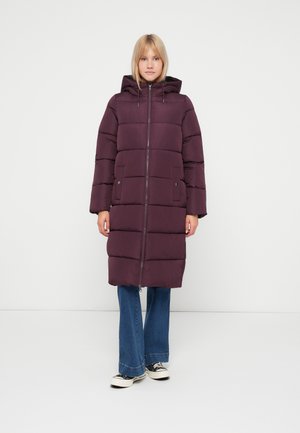 Manteau matelassé violet avec capuche, présentant des panneaux cousus horizontalement, fermeture éclair à l'avant et poches latérales, porté sur un jean évasé et des baskets.