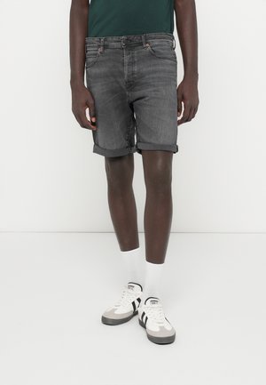 Pantalones cortos de mezclilla gris con dobladillos enrollados, cinco bolsillos y cierre de botón metálico. Combinados con calcetines blancos y zapatillas en blanco y negro.