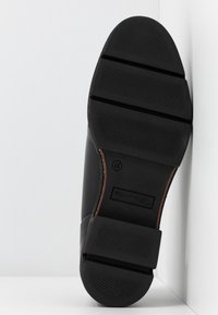 Semelle noire d'une chaussure de ville avec une bande de roulement texturée et deux rainures horizontales, taille 37 visible près de la zone de la voûte plantaire.