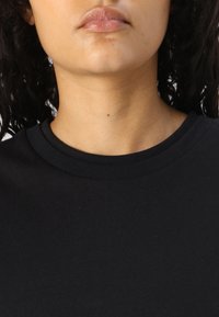 Juoda medvilnės marškinėlių su apvaliomis kaklo iškirptėmis bet kas, su groove, lygia tekstūra, demonstruojanti minimalistinį dizainą be papildomų raštų ar akcentų.