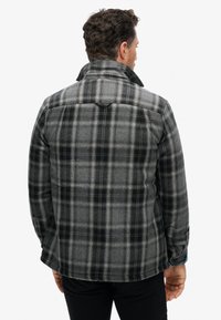 Veste à carreaux gris avec des accents noirs, dotée d'un col et de poignets boutonnés. Fabriquée dans un tissu texturé pour plus de chaleur. Vue de dos.
