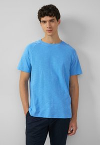 Blauwe T-shirt met korte mouwen van gestructureerde stof. Heeft een ronde halslijn en raglanmouwen. Gedeeltelijk met casual marineblauwe broek.
