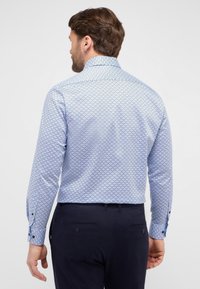 Hellblaues Hemd mit geometrischem Muster, langen Ärmeln und Button-Down-Kragen. Der verwendete Stoff hat eine glatte Textur.