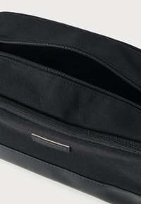 Μαύρη υφασμάτινη θήκη με δύο ανοικτά φερμουάρ και μια μικρή ραμμένη ετικέτα στο μπροστινό μέρος.