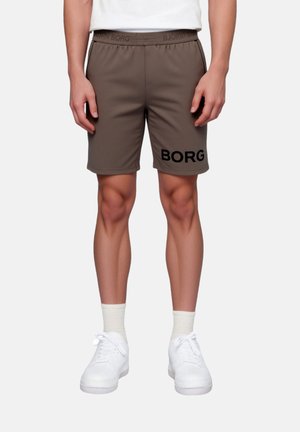 Barna rövidnadrágot viselő lábak "BORG" felirattal a bal combon, fehér zokniban és fehér tornacipőben, egyenes állásban sík háttér előtt.