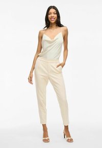 Cami-top in lichtcrème met dunne bandjes, gecombineerd met lichtbeige op maat gemaakte broek met zijzakken en een taps toelopende pasvorm. Strappy hoge hakken.