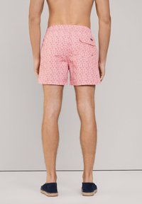 Costume da bagno rosa con motivo a foglie di palma, vita elastica e tasca posteriore; indossato con espadrillas blu navy. Tessuto morbido.