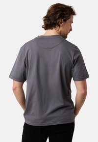 Harmaa puuvillapaidan t-paita lyhyillä hihoilla, pyöreällä kauluksella ja hienovaraisilla ompeluyksityiskohdilla kaula-aukossa, näkymä takaa.