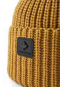 Cappello a maglia giallo senape con texture a costine. Presenta una toppa quadrata nera con una foglia d'acero e la scritta "CANADIAN" in rilievo.