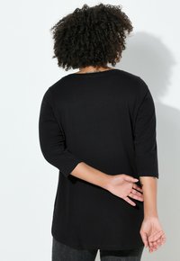 Černá košile s tříčtvrtečními rukávy, volným střihem, hladkou texturou a kulatým výstřihem, pohled zezadu.