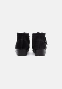 Stivali ankle in suede nero con una finitura testurizzata, punta arrotondata e tacco basso a blocco. Presentano cuciture sulla tomaia e un dettaglio a frangia.